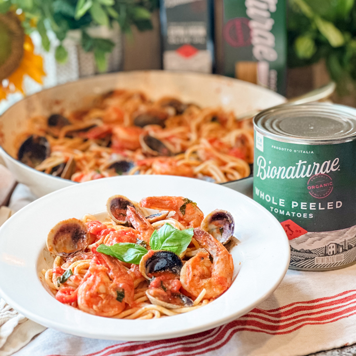 A plate of Clam and Shrimp pasta next to a can of Bionaturae Whole Peeled Tomatoes